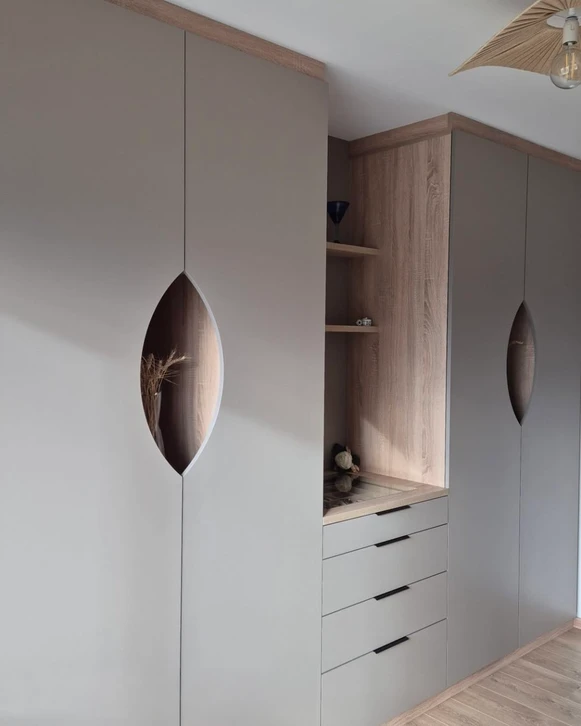 Chambre moderne avec dressing ouvert intégré au mur, lit double avec linge gris et blanc, fauteuil scandinave beige, luminaire articulé noir