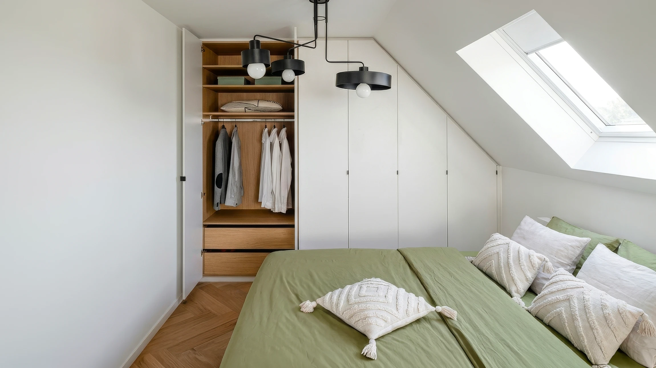 Chambre moderne sous combles avec lit blanc, coussins géométriques noirs et blancs, bureau en bois avec chaise grise, horloge murale, échelle décorative, suspension en rotin