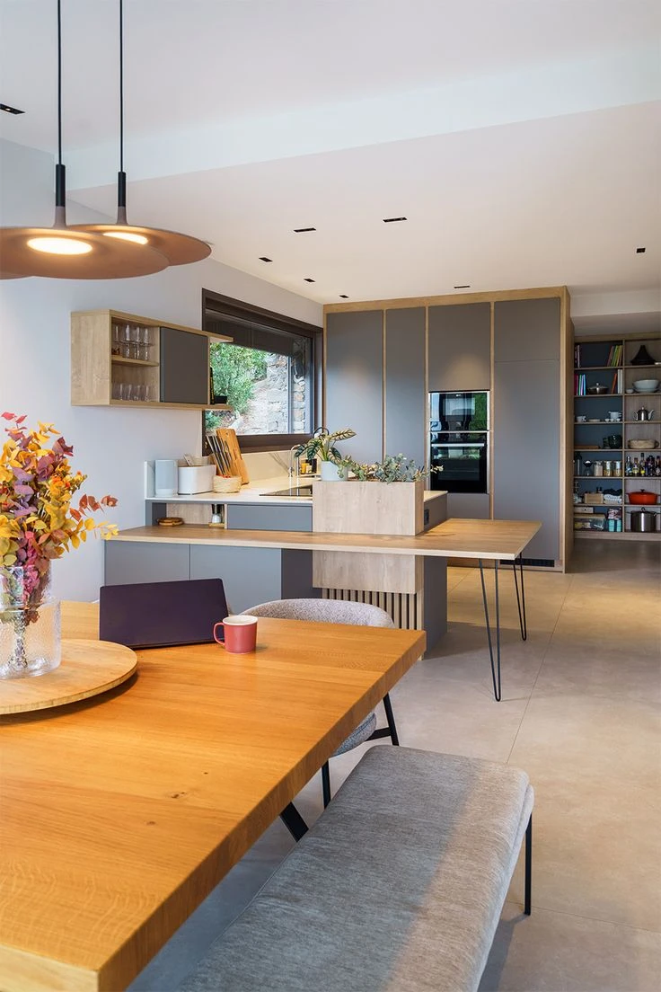 Salle à manger élégante avec table ronde en bois foncé et six chaises rembourrées disposées dans un coin fenêtré